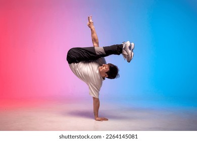 dancer doing acrobatic stunts and dancing break dance in neon red and blue light, young energetic guy stands on his hands in an unusual pose and shows his hand up, street style
