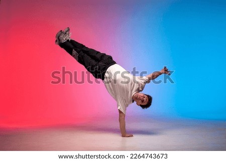 dancer doing acrobatic trick and dancing breakdance in neon red and blue lighting, young energetic guy stands on his hands in unusual pose, street style, copy space