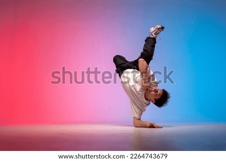 dancer doing acrobatic trick and dancing breakdance in neon red and blue lighting, young energetic guy stands on his hands in unusual pose, street style, copy space