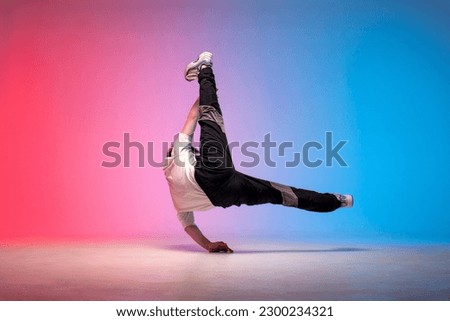 dancer doing acrobatic trick and dancing breakdance in neon red and blue lighting, young energetic guy stands on his hands in unusual pose, street style