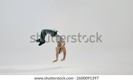 Dancer, dressed casual clothes, arching backwards mid-air, frozen in moment of flight and precision against white background. Concept of breakdance, dance, music, artistic movement, acrobatics, sport.