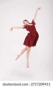 Dancer performs a jump while wearing a red dress in a studio with plain background during a dance session