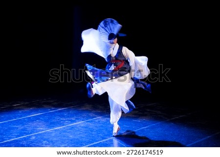 Dancer performs traditional dance on stage with fan during cultural event at local theater in the evening
