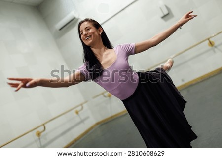 A dancer is practicing in a dance studio. She stands on one leg with her arms extended. The walls are plain and the mirrors reflect her movements as she enjoys her routine.