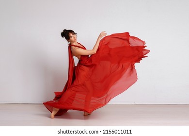 Dancer in a red flying dress. Woman ballerina dancing on a white studio background