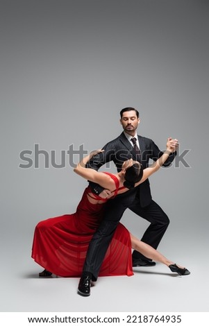 Dancer in suit performing tango with elegant partner on grey background