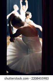 Dancer Thinking Backstage At Ballet Concert Or Recital While Group On Theater Stage. Girl Ballerina Waiting On Floor Of Auditorium, Anxiety And Nerves, For Performance In Front Of Audience Or Crowd