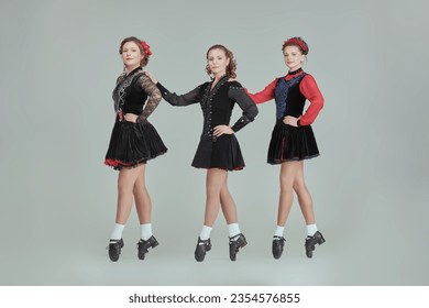 Dances. Irish ensemble of three beautiful women in concert costumes and Ghillies Hard Shoes dance together in a row. Full-length studio portrait on a grey background. - Shutterstock ID 2354576855