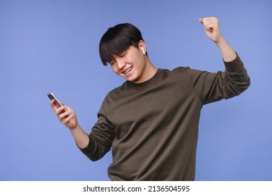 Dancing active asian korean young man boy student listening to the music on cellphone using earbuds, choosing soundtrack, playlist, radio isolated in blue background - Shutterstock ID 2136504595