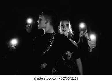 Dancing Couple Of Boy And Teenage Girl Posing Ballroom Dancing With People In The Background Taking Photos With Their Phones And Flashes