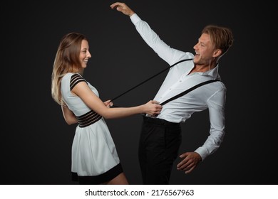 Dancing Couple In White Dress And Shirt In Studio Stand In Studio While Woman Pull At Suspenders Of Man To Hold Him When He Lose Balance