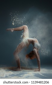 Dancing in flour concept. Redhead beauty gymnast female girl adult woman dancer in dust / fog. Girl wearing white top and shorts making dance element in flour cloud on isolated grey background