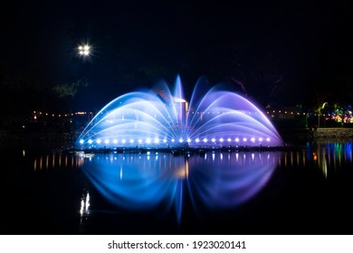 A dancing fountain or a fountain that is formed by controlling the ups and downs and has a light tone bright blue and purple.  And the color reflecting on the water.