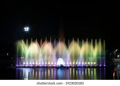 A dancing fountain or a fountain that is formed by controlling the ups and downs and has a light tone green bright and purple.  And the color reflecting on the water.