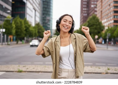 Dancing girl feeling happy in city. Asian woman dancing and listening music in headphones, posing on street. - Powered by Shutterstock