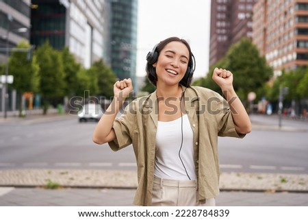 Dancing girl feeling happy in city. Asian woman dancing and listening music in headphones, posing on street.