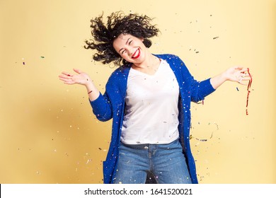 Dancing And Laughing Beautiful Young Woman Plus Size In Jeans And Blue Sweater. Yellow Background. Close-up.