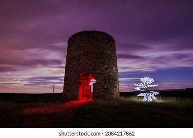 Dancing at the mill. Old windmill illuminated with red light at the entrance and with a beautiful white light shape with lightpainting photographic technique.