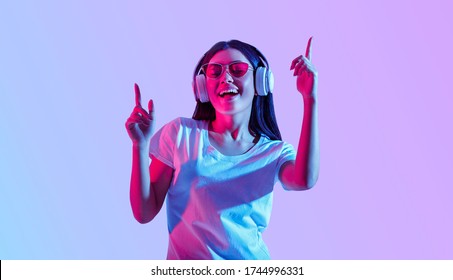Dancing in modern wireless headphones. Asian girl with glasses enjoys favorite song, isolated in neon, studio shot - Shutterstock ID 1744996331