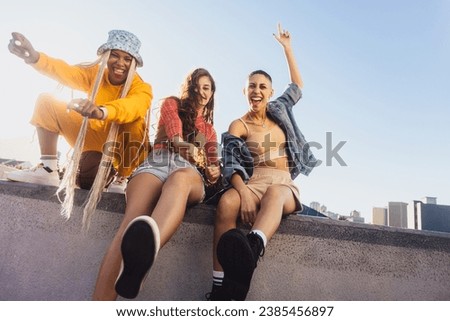 Dancing on the wall. Three vibrant female friends dancing cheerfully while sitting together on a wall in the city. Group of multiethnic youngsters having fun and enjoying themselves.