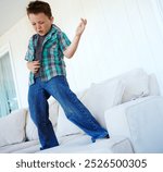 Dancing, play or boy with air guitar on sofa for comedy, humour or funny joke for rock and roll. Happy, excited kid or crazy child with music, celebration or imaginary instrument on couch in home