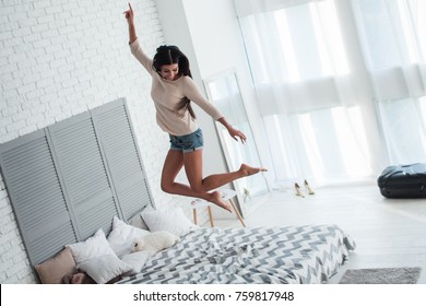 Dancing queen in the morning. Full length of beautiful young woman jumping on bed with smile indoors