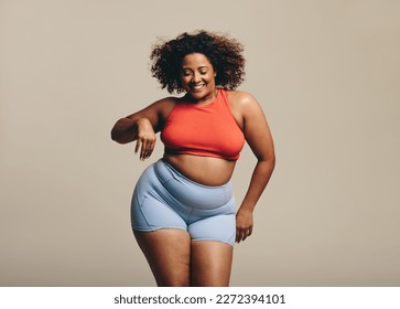 Dancing in a studio with confidence, a plus size woman proudly shows her sportiness and flexibility in sportswear. Happy young woman celebrating body positivity and embracing fitness.