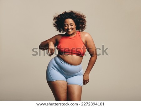 Dancing in a studio with confidence, a plus size woman proudly shows her sportiness and flexibility in sportswear. Happy young woman celebrating body positivity and embracing fitness.