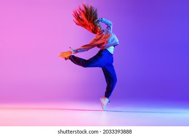 Dancing style. Young beautiful girl expressively making hip-hop tricks on gradient neon background. Youth culture, style and fashion. Concept of dance, youth, hobby, dynamics, movement, action, ad