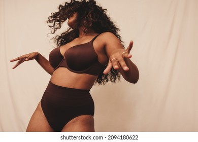 Dancing in underwear. Cheerful young woman having fun while wearing brown underwear against a studio background. Confident young woman celebrating her natural body in a studio.