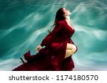 Dancing woman under the water in a pool in a red dress.