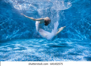Dancing woman under the water in a pool in a white dress, she is like a Rusalka. Surrealistic photography.