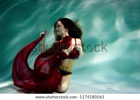 Dancing woman under the water in a pool in a red dress.