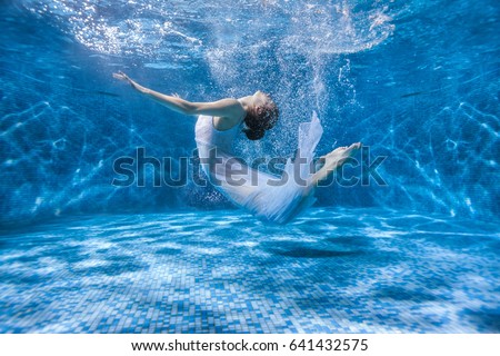 Dancing woman under the water in a pool in a white dress, she is like a Rusalka. Surrealistic photography.