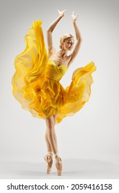 Dancing Woman in Yellow Dress. Ballerina in Shoes Dance Modern Art Ballet over Light Gray Background. Graceful Girl Stretching Hands up