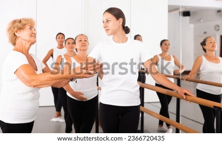 Dancing women engaged in classical ballet at a group training session in the studio stand in a ballet stance, where the ..choreographer helps to coordinate the movement correctly