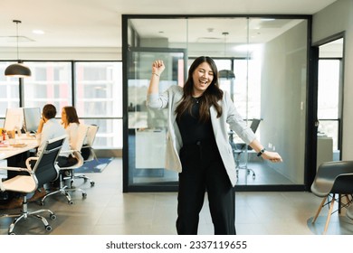 Dancing young asian businesswoman celebrating salary raise in office - Powered by Shutterstock