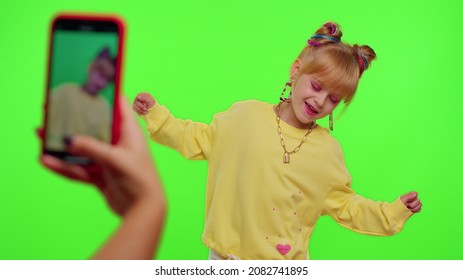 Dancing young little kid girl blogger record dance moves at camera for social media content using phone indoors on chroma key green screen background. Children schoolgirl perform trendy funny dance - Shutterstock ID 2082741895
