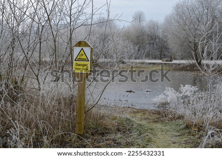 'Danger Deep water' sign beside a frozen pond on a frosty winter day. UK