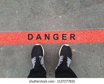 Danger. Man Legs In Black Shoes Standing Behind The Red Line