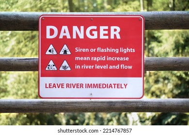 Danger sign about fast rising water on hiking trail bellow a dam. Signage with safety instruction in case of hearing sirens at the river. Cleveland dam, North Vancouver. BC, Canada. Selective focus.