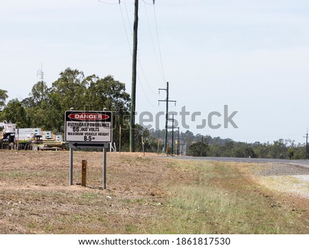 A danger sign on a highway turnoff warning of high voltage powerlines and maximum vehicle height.