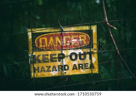 Danger sign with text KEEP OUT HAZARD AREA as warning message hanging on fenced dark zone, dirty poster outside.