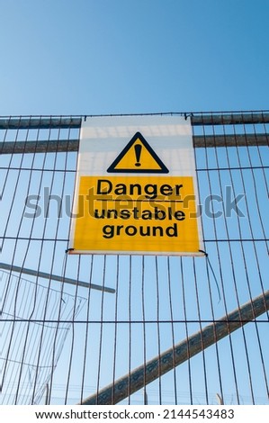 Danger unstable ground sign on a fence against a blue sky