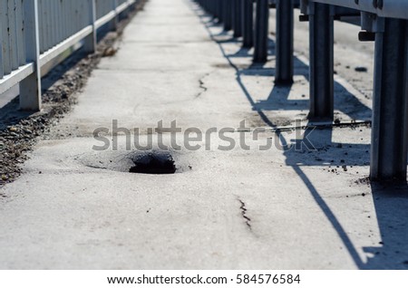 Dangerous damage on the bridge with deep hole between security metal fence on the pedestrian walkway with danger that someone will step in the hole or damage the bicycle wheel in the lane