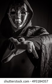 Dangerous dark hooded and masked assassin reaching out his hand