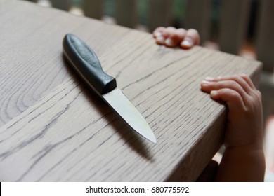 Dangerous hazardous  in the kitchen.Kitchen knife put on table. 1 year baby boy standing and trying to get a kitchen knife. Hazards for home health-care,common  dangers for kid at home.Selective focus - Shutterstock ID 680775592