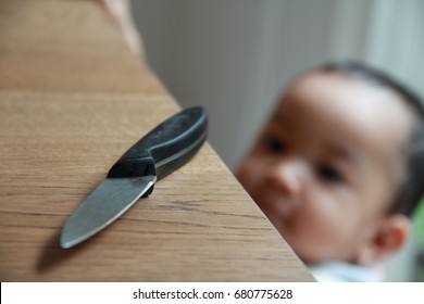 Dangerous Hazardous  In The Kitchen.Kitchen Knife Put On Table. 1 Year Baby Boy Standing And Trying To Get A Kitchen Knife. Hazards For Home Health-care,common  Dangers For Kid At Home.Selective Focus