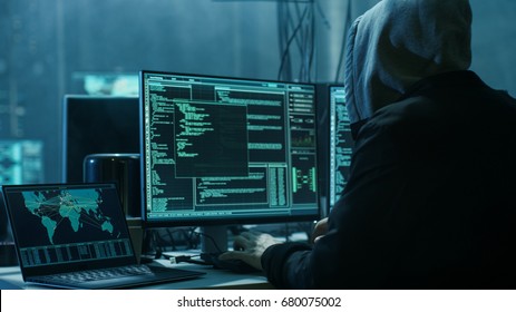 Dangerous Hooded Hacker Breaks into Government Data Servers and Infects Their System with a Virus. His Hideout Place has Dark Atmosphere, Multiple Displays, Cables Everywhere. - Shutterstock ID 680075002