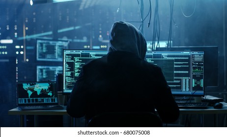 Dangerous Hooded Hacker Breaks into Government Data Servers and Infects Their System with a  Virus. His Hideout Place has Dark Atmosphere, Multiple Displays, Cables Everywhere.